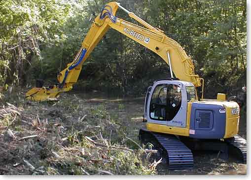 excavator crawling up streambed while mulching drainage vegetation